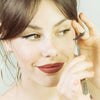 Jeune femme brune, 25 ans, au teint clair, elle tient la pince du kit d'application FADIME, faux cil en chanvre 100% végétal, biodégradable, bandes transparentes en coton. Émerveillée, amène la pince vers son œil. Avec tracé magnifique et précis BlackFadime, eyeliner adhésif 2 en 1 noir. Haute précision, tenue parfaite, Waterproof, végan, fixation rapide, tenue durable. Polymères doux et durables, haute qualité, hypoallergéniques. Flexibles, confort sans paraben, idéal yeux sensibles. ultra précis