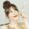 Une jeune femme brune de 25 ans, au teint clair, elle tient de la main gauche le packaging du stylo eyeliner adhésif transparent le Clearfadime de FADIME et tien de la main droite le packaging du BlackFadime eyeliner adhésif 2en1 noir en regardant avec amusement le Clearfadime . Sa pointe fine et feutre souple garantie haute précision. Waterproof, végan, il assure une tenue parfaite et une rapide fixation grâce aux polymères naturels. Hypoallergénique. Un allié ultra précis