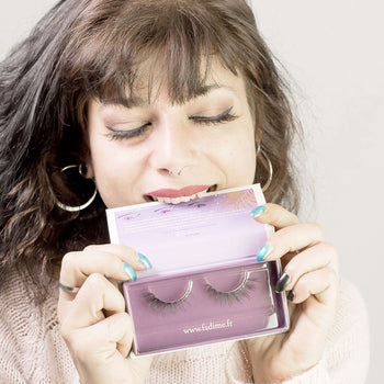 Une femme méditerranéenne de 30 ans, brune, qui serre entre ses dents  les Faux cils naturels effet  Harmonieux de Fadime, naturels en fibres de chanvre 100% végétales et biodégradables. Végan, doux, durables, d'une qualité exquise. Hypoallergéniques et sans paraben, ils conviennent aux yeux sensibles. Leur épaisseur et leurs bandes transparentes en fibres de coton offrent un confort flexible et une tenue parfaite. Réutilisables jusqu'à 40 fois. La beauté responsable à son apogée.