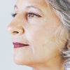 À 55 ans, cheveux grisonnants, elle sourit et regarde à droite, elle porte les Faux cils naturels effet naturel de Fadime en fibres de chanvre 100% végétales et biodégradables. Végan, doux, durables, d'une qualité exquise. Hypoallergéniques, sans paraben, conviennent aux yeux sensibles. Épaisseur et bandes transparentes en fibres de coton pour confort et tenue. Réutilisables jusqu'à 40 fois.